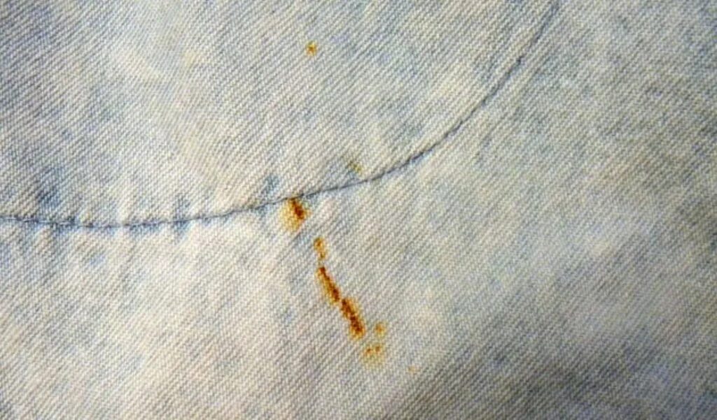 Пятно на ткани. Ржавчина на одежде. Ткань в крапинку. Ржавое пятно на ткани.