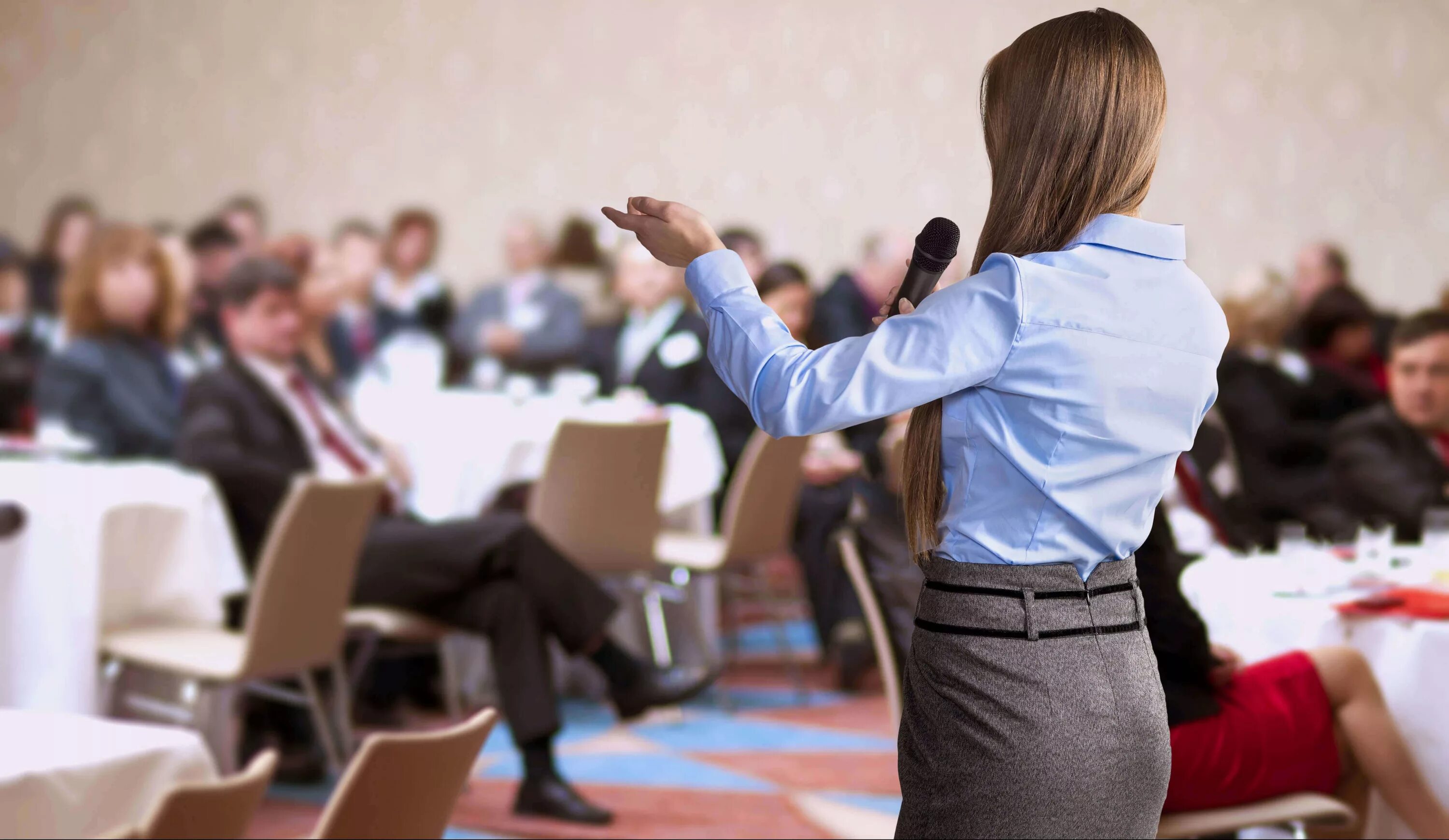 Женщина оратор. Спиной к аудитории. Женщина выступает перед публикой. Человек за трибуной. Успешный оратор.