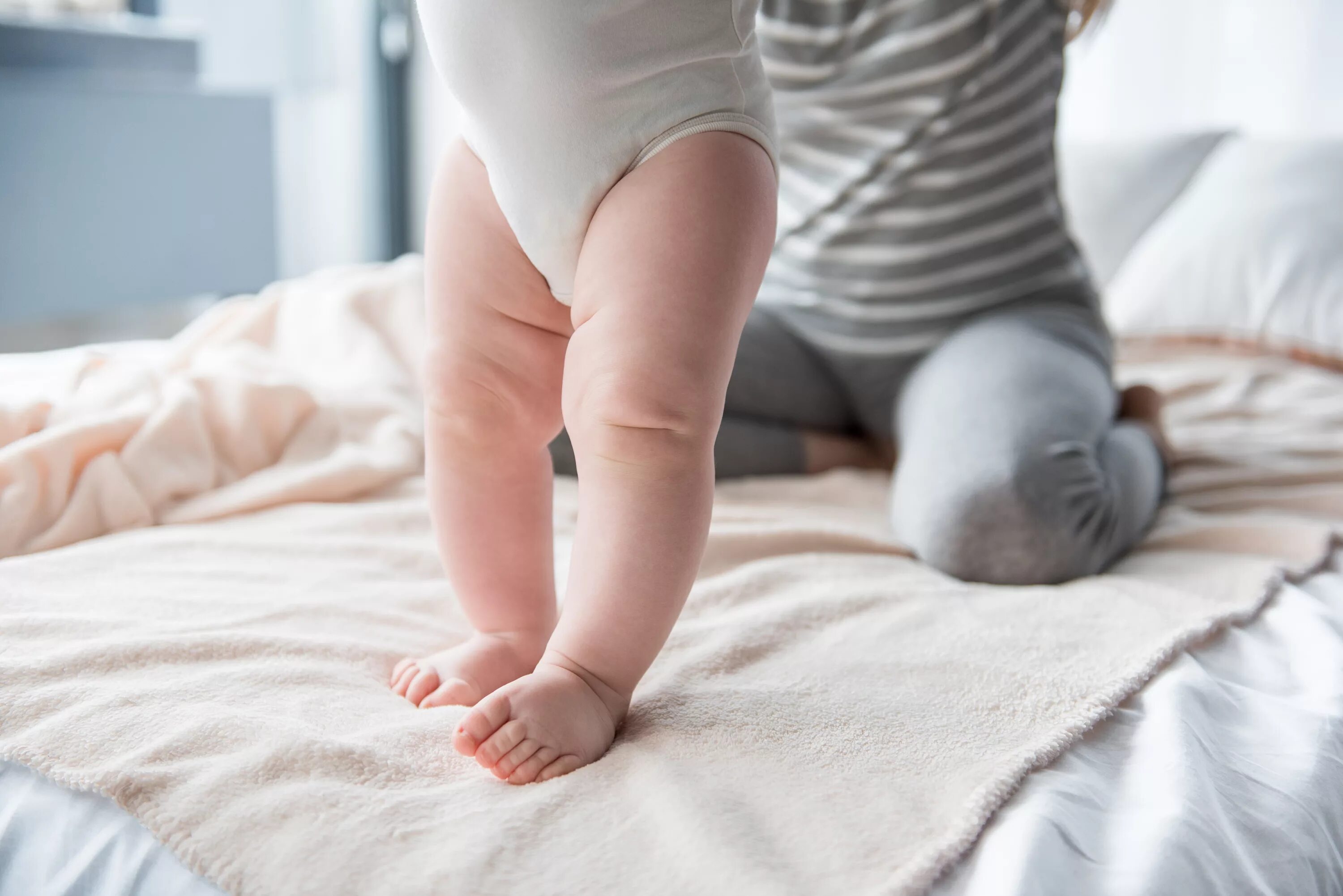 Ножки в 6 месяцев. Младенец стоящий на ногах. Опора на ножки у грудничков.