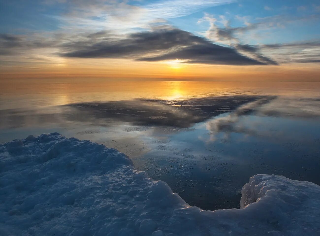 зимний океан. зимний закат над островом. валуны на снегу. снег и солнце. закат на море.