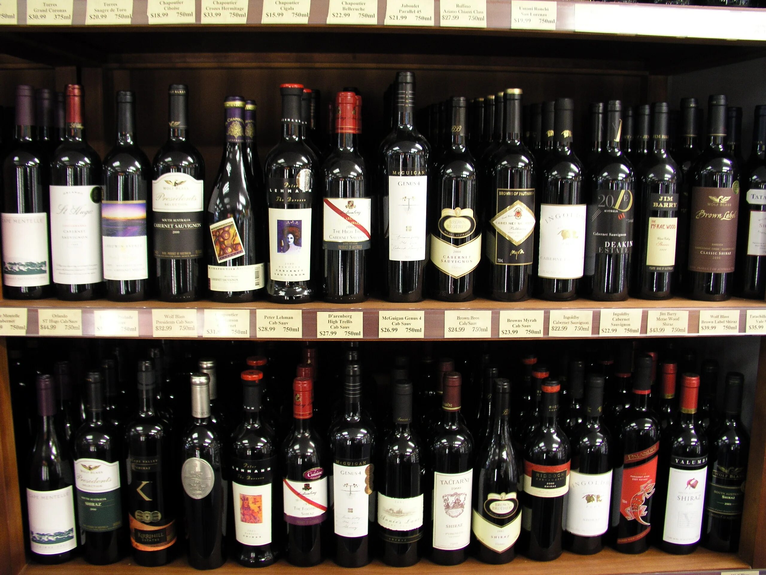 Купить вино в магазине красное. Винный прилавок. Витрина с вином. Вино на полках в магазинах. Бутылка вина.