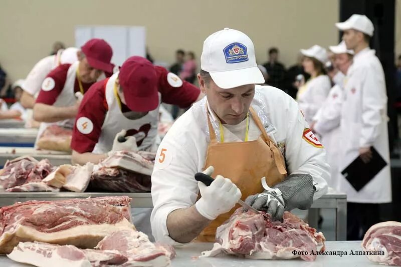 Portrait of a handsome butcher in white uniform at the meat manufacturing with p