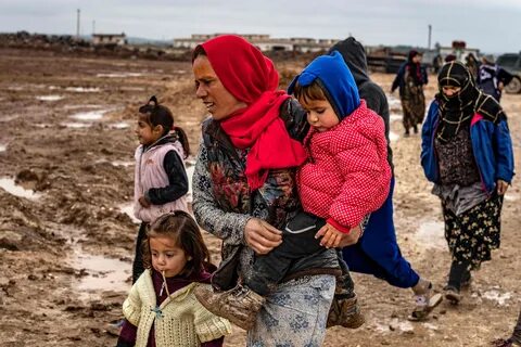 Syrian women accompany children in a muddy field in the Washukanni Camp for...