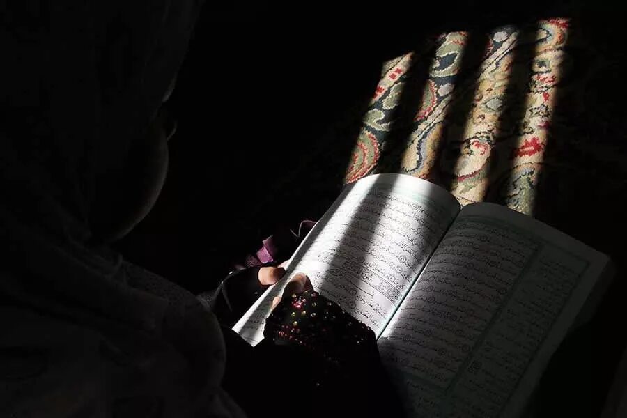 Полный коран читает. Коран читать. Коран в темноте. Коран в руках девушки. Девушка читает Коран.