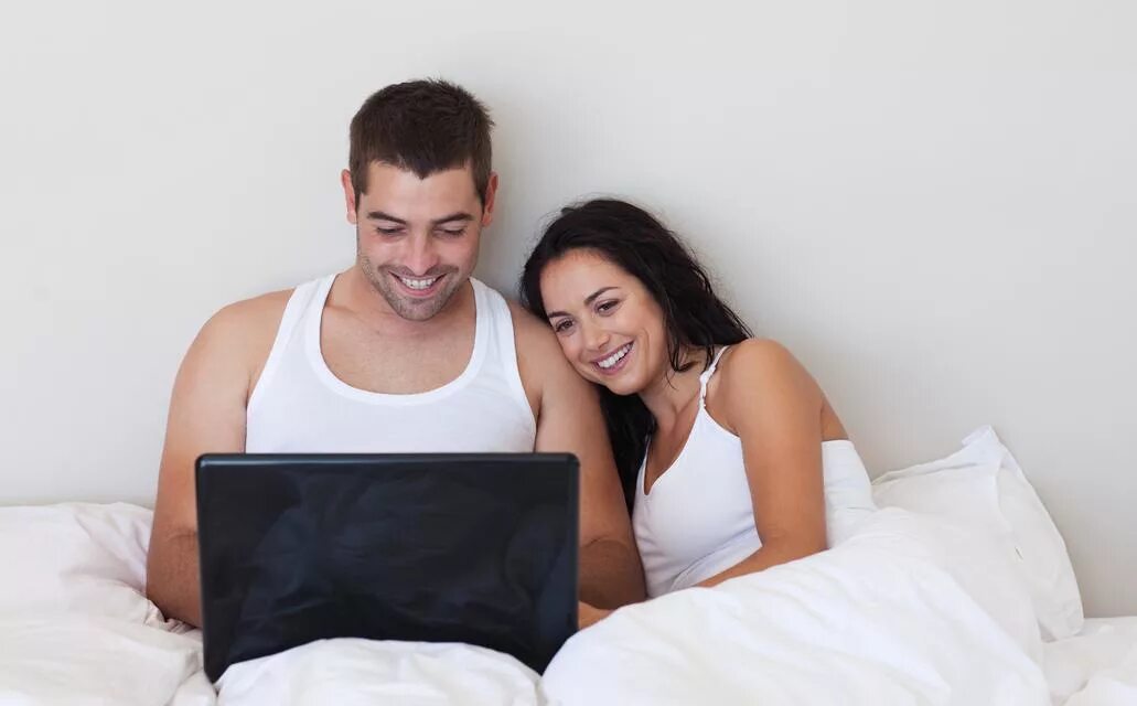 Жена связала мужа русское. Пара на кровати с ноутбуком. Счастливая пара сидит на кровати. Муж с женой в кровати Сток. Муж с женой сидят за компьютером.