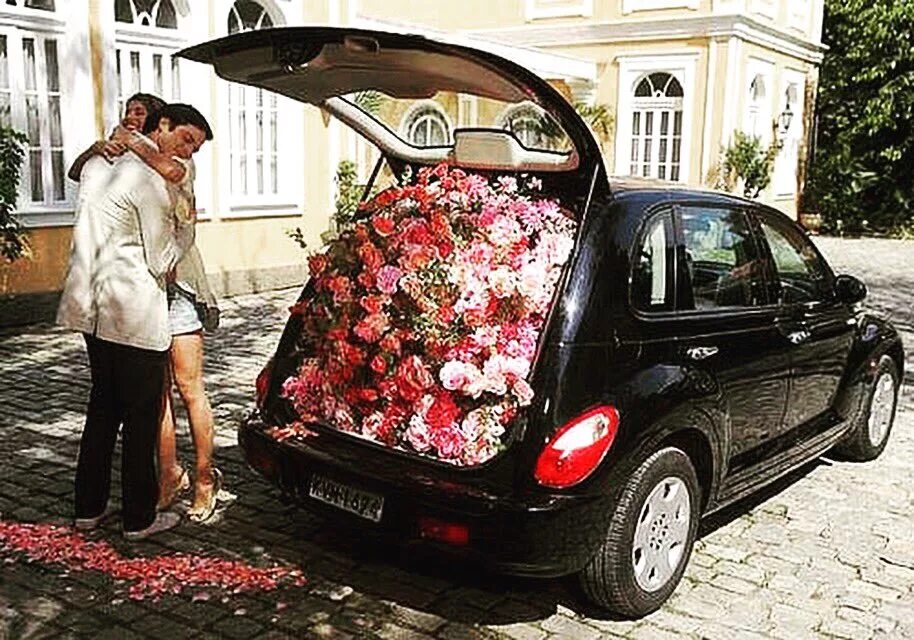 Сюрприз в машине. Мужчина дарит машину девушке. Цветы в багажнике машины. Машина с цветами. Дорогие подарки для женщин.