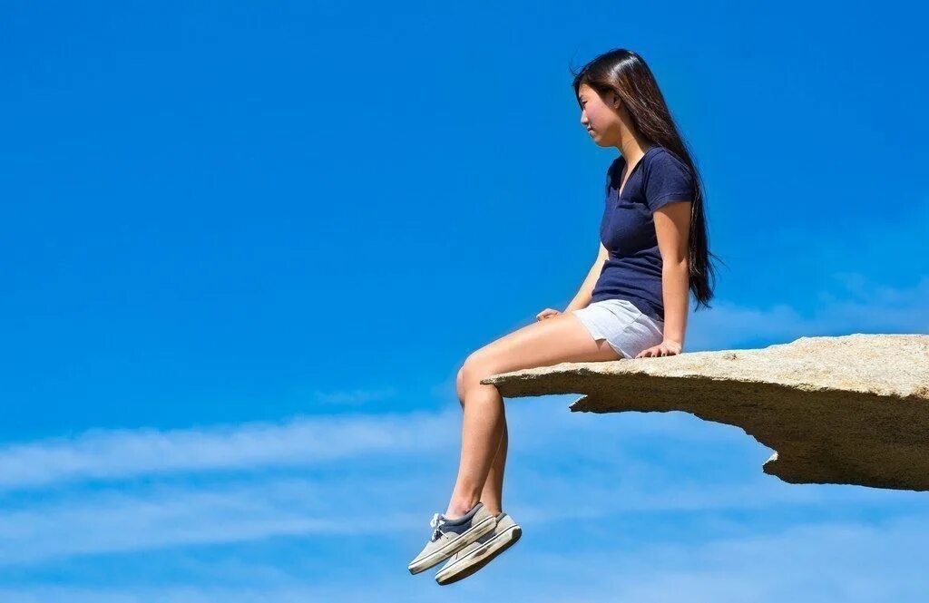 Девушка сидит на обрыве. Девочка сидит на скале. Девушка сидит свесив ноги. Ходим по краю но не видим края