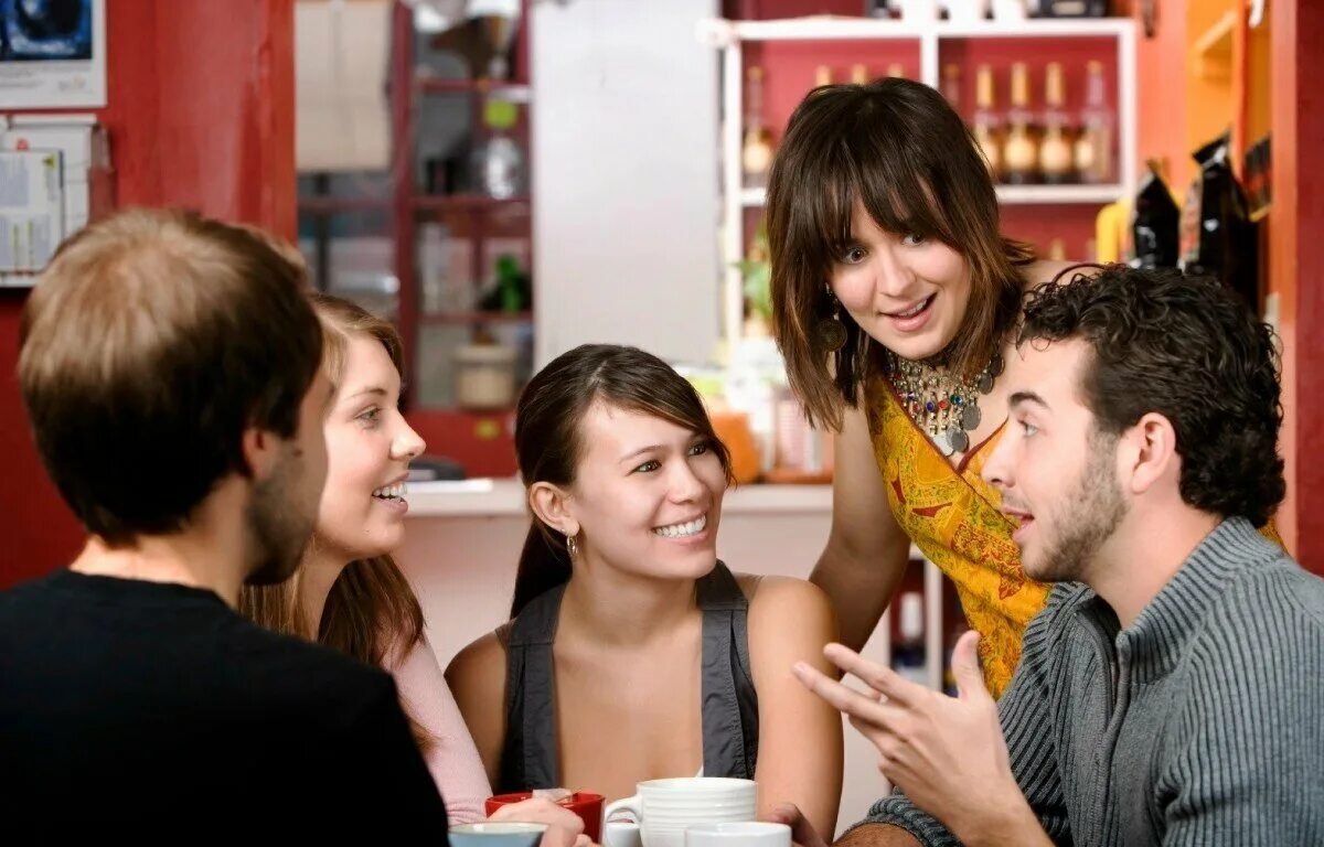 Давайте друг друга разговариваете. Друзья и встречи. Разговоры с друзьями. Живое общение. Подростки за столом в кафе.
