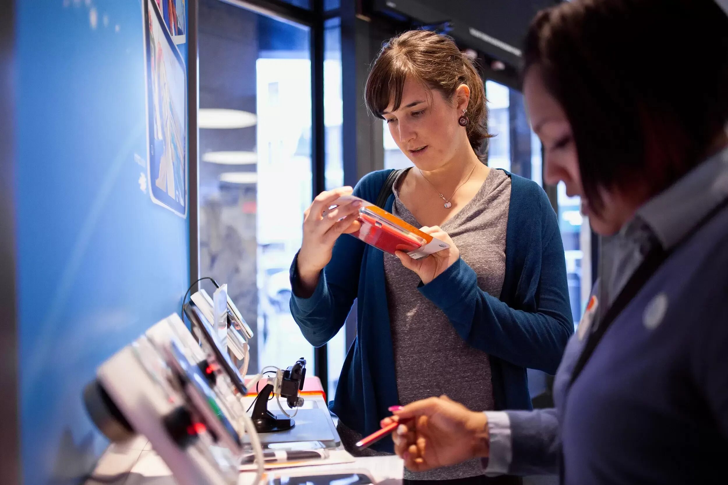 Девушка показывает смартфон. Человек покупает телефон. Выбор смартфона в магазине. Человек со смартфоном. Смартфоны на прилавке.