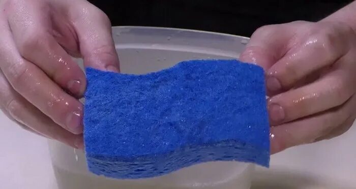 Рука выжимает губку. Губка в воде. Губка для мытья мокрая. Рука выжимает губку. Губка в воде.
