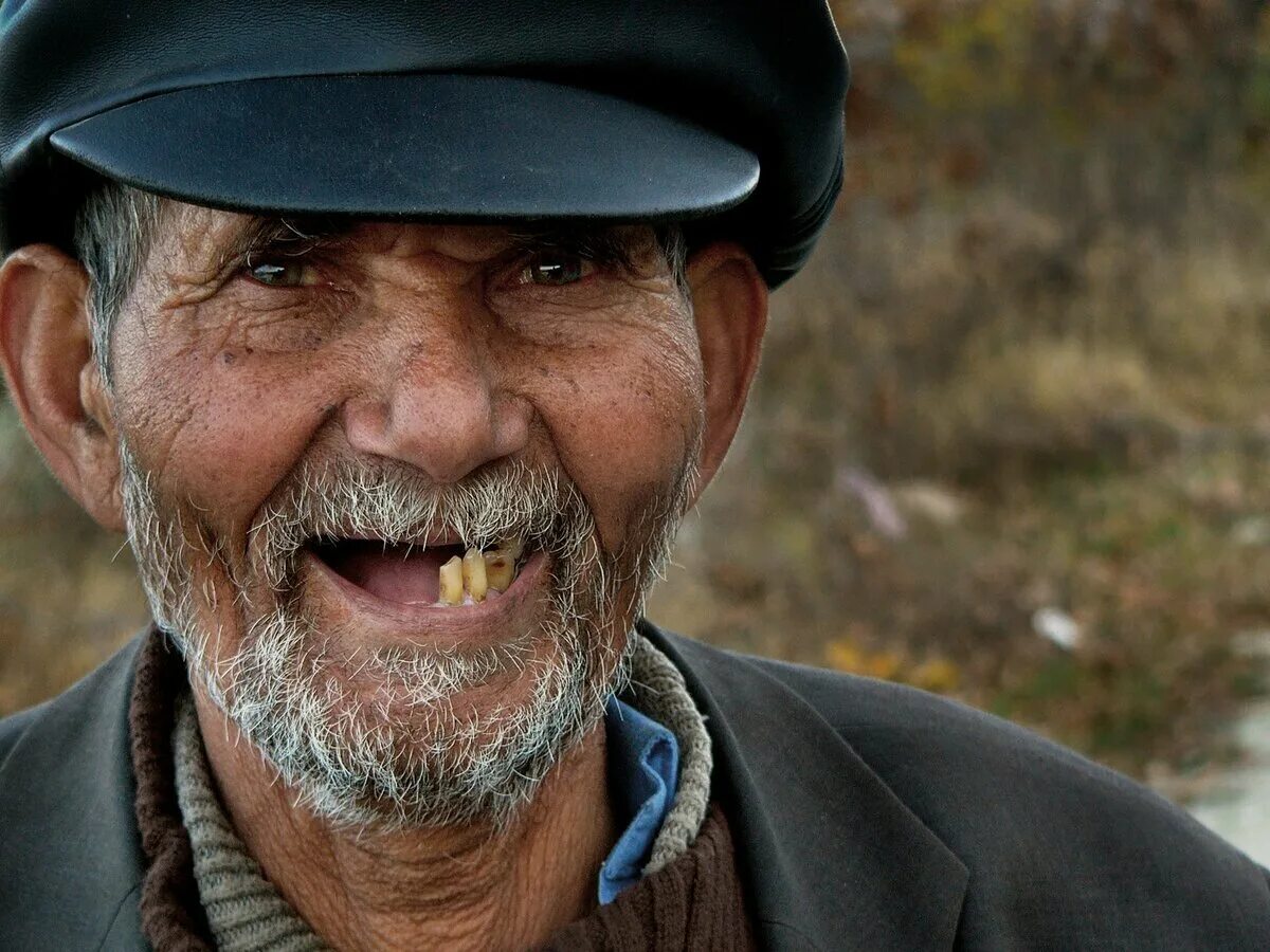 Улыбается без зубов. Беззубая улыбка старика. Дряхлый старик.