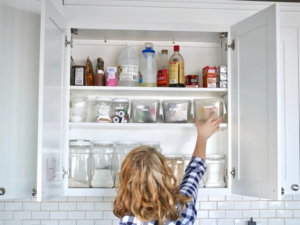 There are two glasses in the cupboard. Open Cupboard. Kitchen Cupboard Jar open. Watervunder the Cupboard. Cupboard Knife and fork Storage Box Clear.