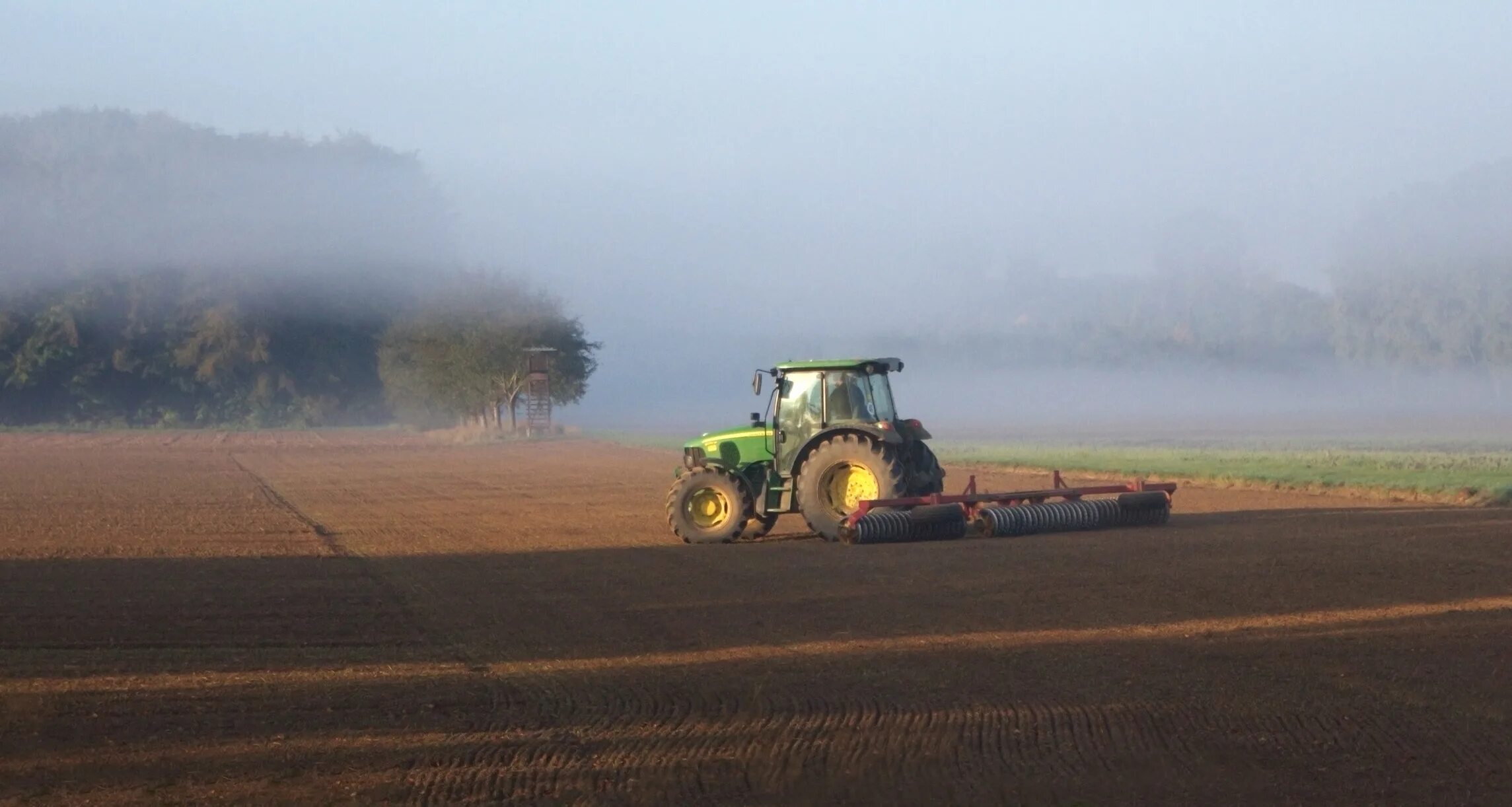 Трактор на пашне. Трактор на поле пашне. Туман в сельском хозяйстве. Пейзаж с трактором.
