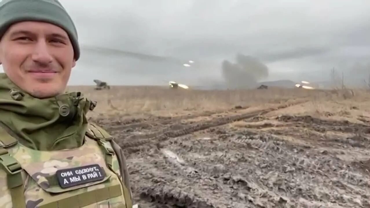 Улыбающийся солдат «народной милиции ДНР» на фоне «Градов», БОМБЯЩИХ. Солдат улыбается.