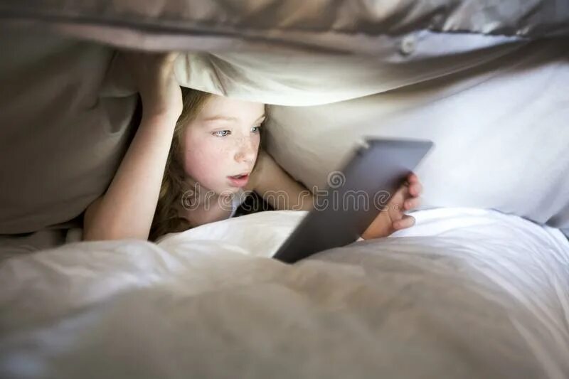 Телефон под одеялом. Маленькая девочка в кровати под одеялом. Девочка с телефоном под одеялом. Ребенок с телефоном под одеялом.