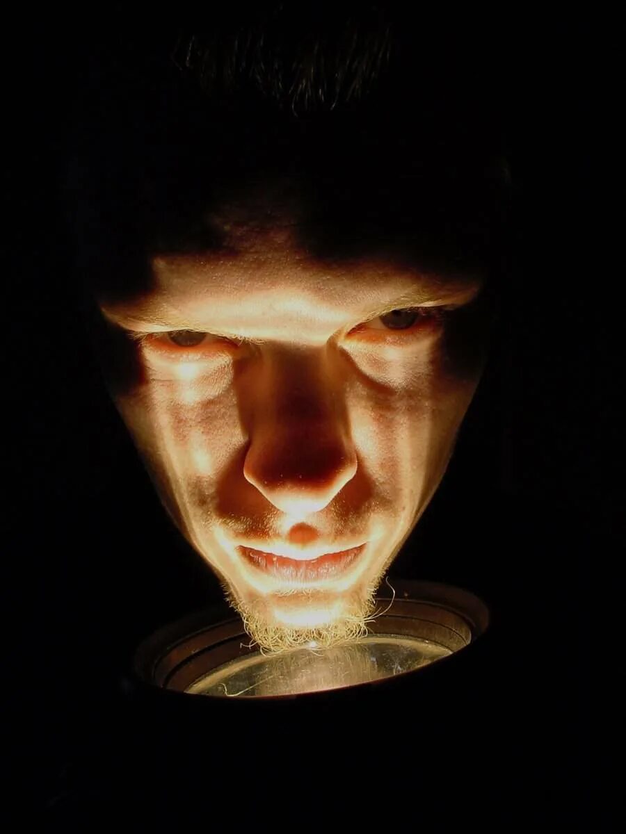 Подсветить лицо. Человек с фонариком в темноте. Фонарик в лицо. Лицо с фонариком в темноте. Светит фонариком в лицо.