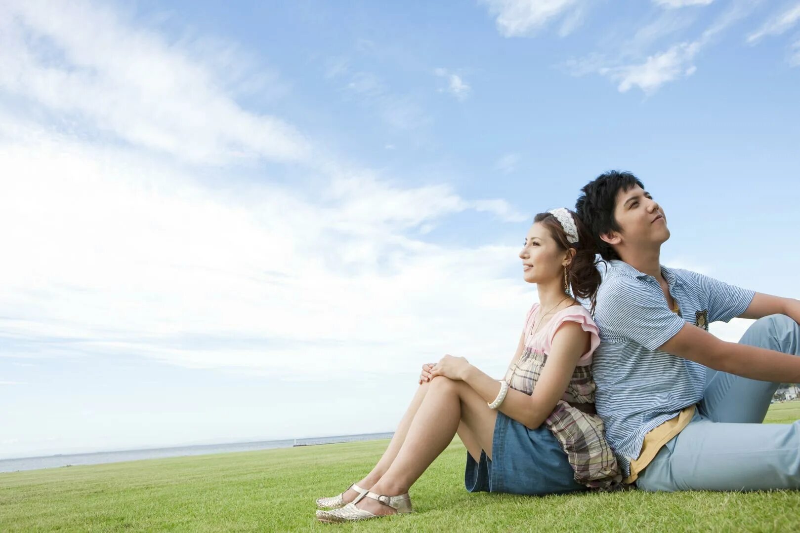 Sitting on the grass. People sitting on the grass. Young man sitting on the ground. Young girl sitting on the ground.