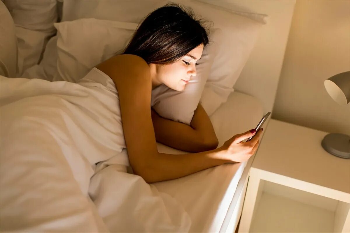 Играть в телефон спать. Человек лежит на кровати с телефоном. Человек с телефоном в кровати. Девушка лежит с телефоном.