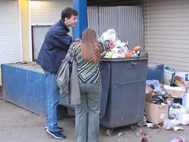 Женщина роется в мусорке. Искать мусорку