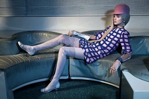 a woman sitting on top of a couch next to a gray chair and wearing a hat 