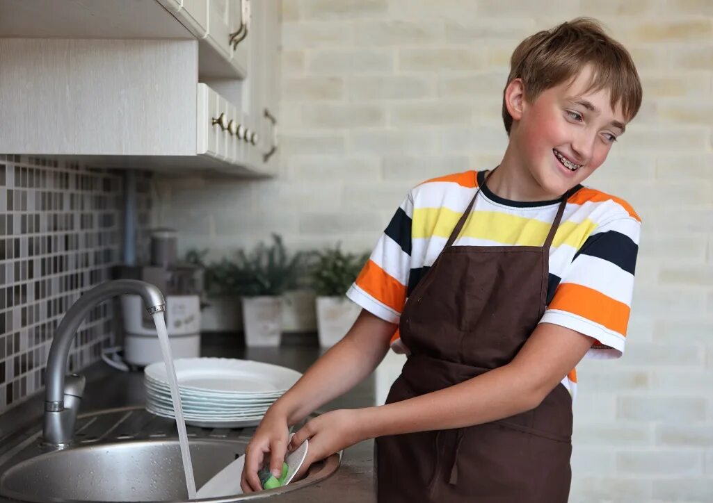 Мальчик моет посуду. Самостоятельный подросток. Самостоятельность подростков. Ребенок помогает по дому. Помогать маме по дому.