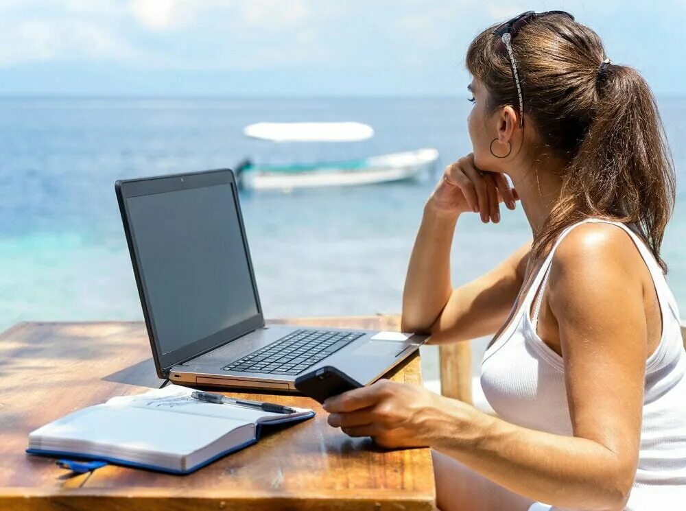 Подработка удаленно. Работать из любой точки мира. Девушка на пляже за компьютером. Удаленная работа фото. Девушка за компом у моря.