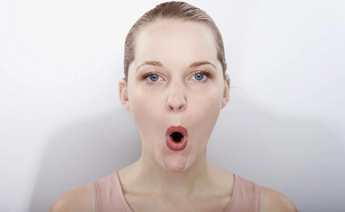 Открытый рот. Удивленные губы. Удивленное лицо девушки. Надутые щеки. Лицо с открытым ртом.