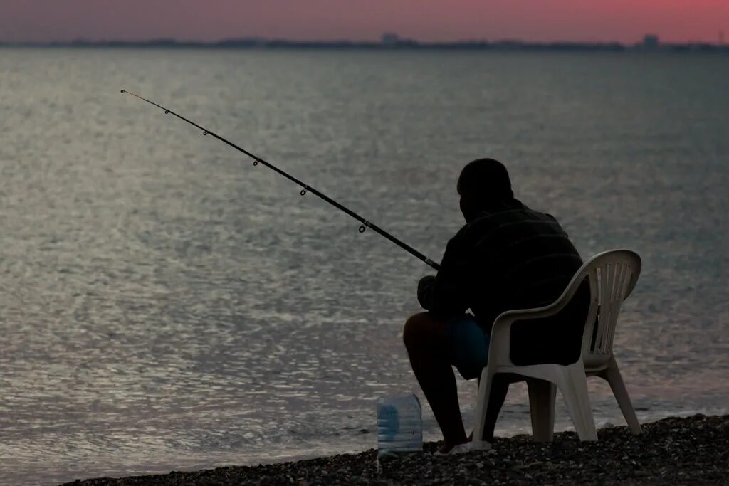 Природа рыбалка. Человек сидит с удочкой. Рыбак сидит. Рыбак на берегу. Мужчина с удочкой на берегу.