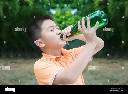 Asian boy drinking water from bottle, in garden, green background Stock Pho...