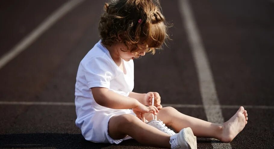 Ребенок завязывает шнурки. Мальчик помогает девочке одеться. Девочка в джинсах завязывает шнурки. Картинка девочка завязывает шнурки. Ребенок завязывает шнурки.