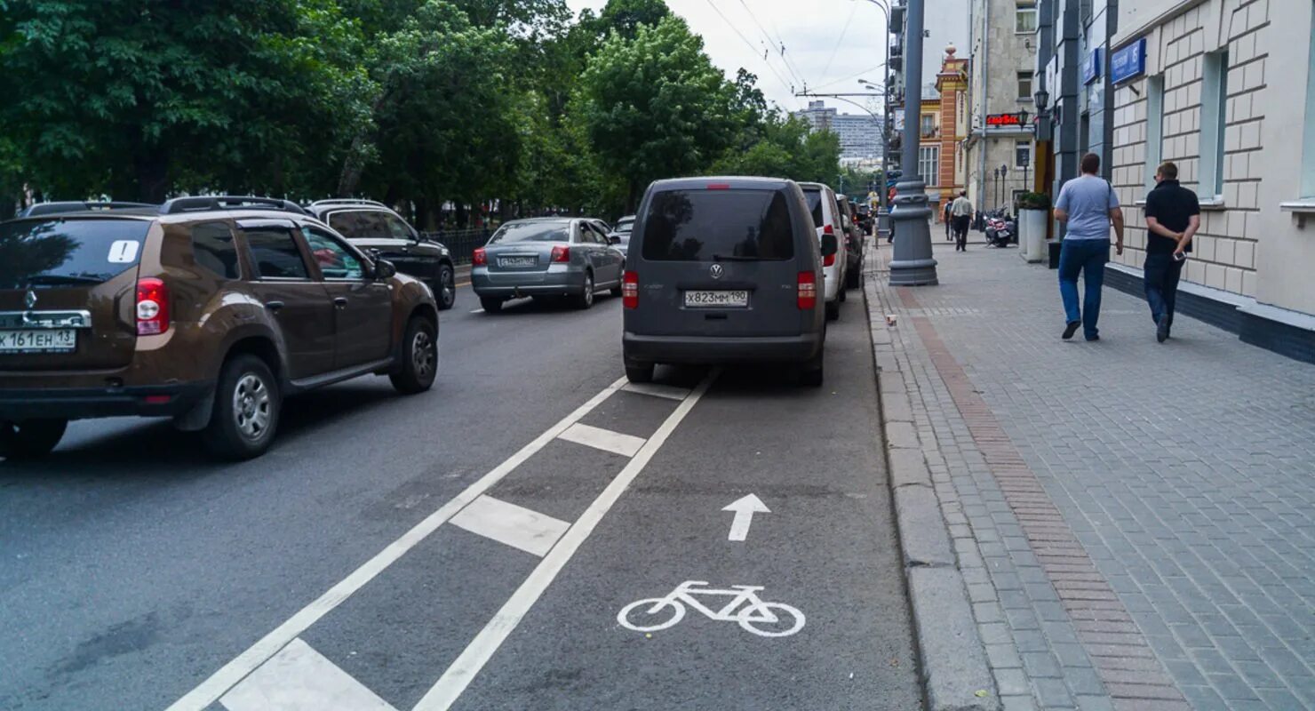 Парковка на велодорожке. Велосипедная дорожка на тротуаре. Пешеход на тротуаре. Машина припаркована на велодорожке.