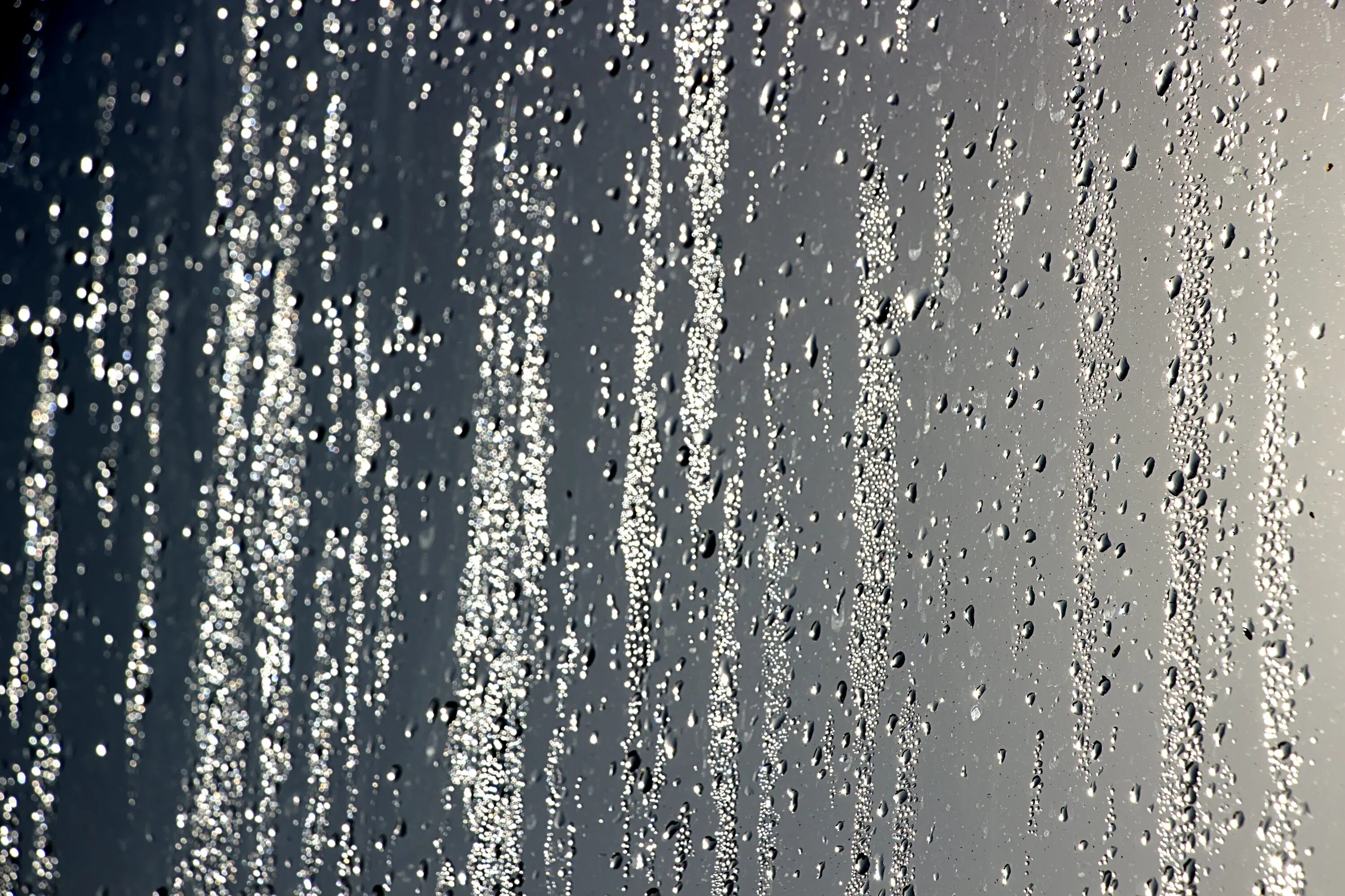 С неба льется вода. Капли на стекле. Капли стекают по стеклу. Струи дождя. Струи дождя на стекле.