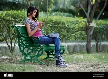 Asian Indian young executive lady driving a car looking at mobile phone Mod...