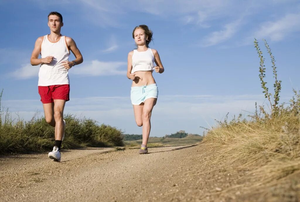 Фото бегущих парня и девушки в белых одеждах. Мужчина и женщина бегут в парке. Спортивная пара. Пара ходов. Красивая пара бежит по полю.