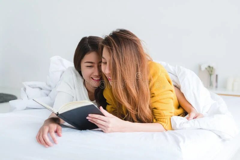 Две девушки под одеялом. Две девушки читают книгу. читает книгу в кровати. женщина читает книгу в постели. совместное чтение книги с девушкой.