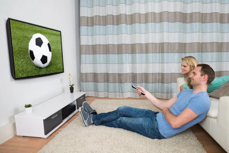 Муж смотрит новости. Футбол по телевизору. Женщина за телевизором футбол. Парень с девушкой смотрят футбол. Диван с телевизором с футболом.