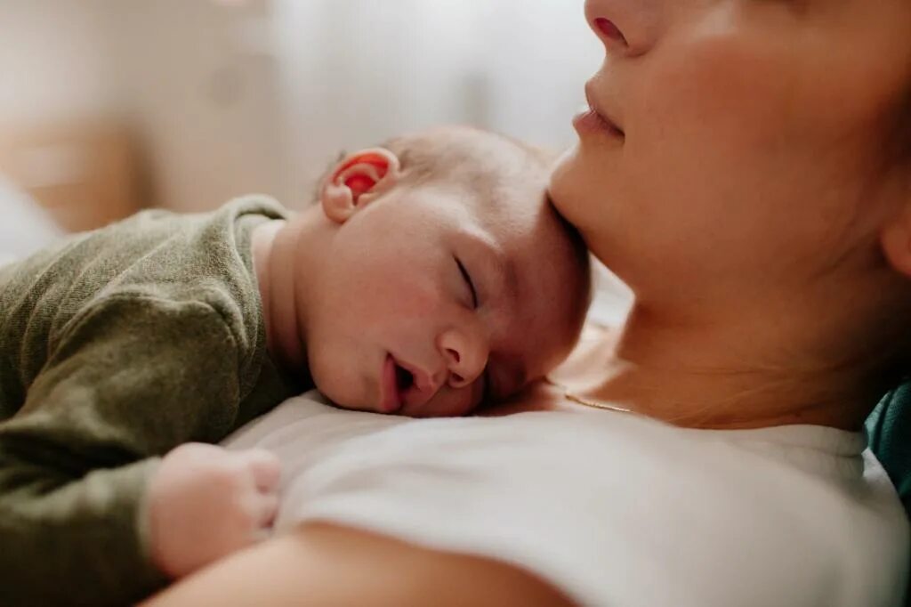 Женщина с грудничком. Мать с ребенком. Улыбающаяся азиатская мама держит в руках ребенка. Месяц материнства. Мамина тревога.