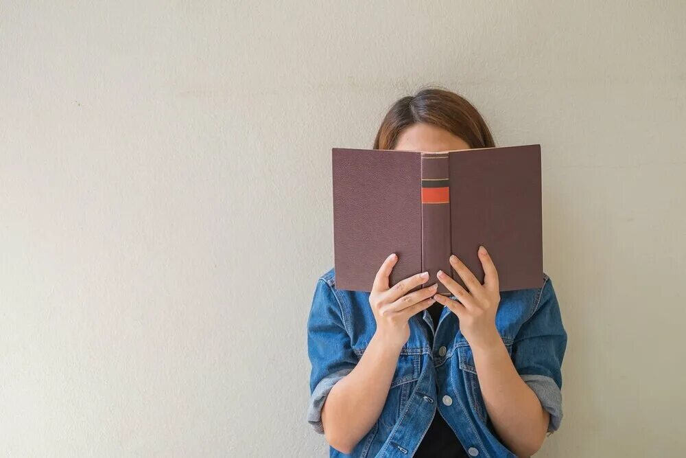 Лицо закрытое книгой. Книжка в руках. девушка держит книгу в руках. человек с книгой в руках. книга в руках.