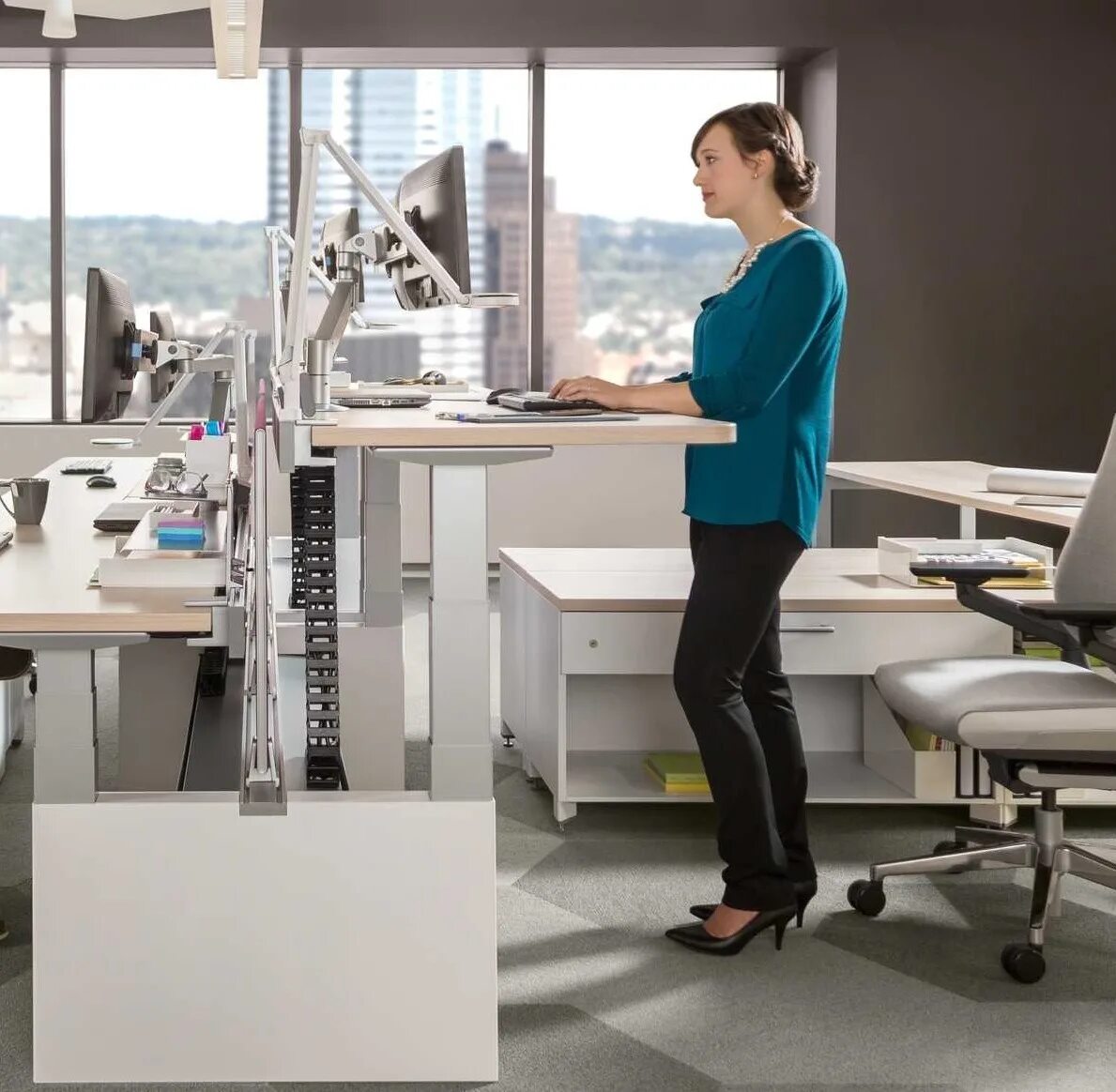 Эргономичное рабочее место в офисе. Ergotron workfit-t, sit-stand desktop workstation. Сидит в офисе. Эргономичное рабочее место. Уютное рабочее место.