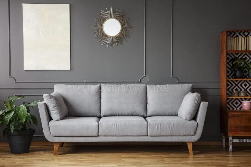 There is a mirror the sofa. Gold sofa near the wall. painting hangs over the sofa.