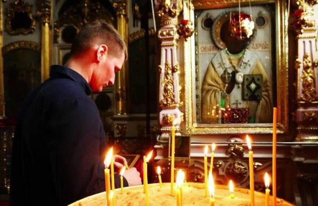 Мужчина ставит свечу. Мужчина молится в храме. Парень молится в церкви. Мужчина у иконы в храме. Молодой человек в храме.