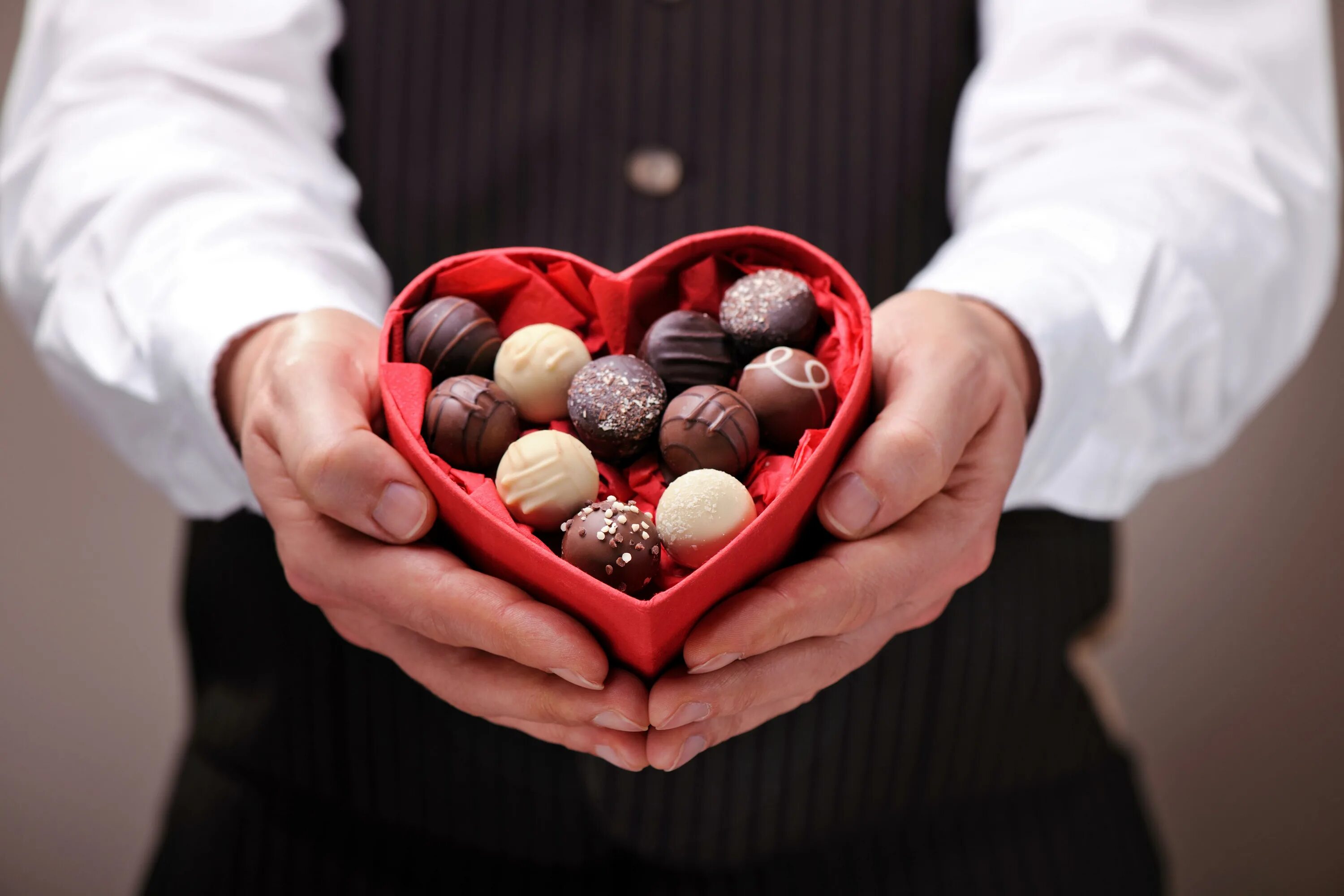Держите в руках сладкое. Коробка шоколадных конфет. Конфета в руке. Шоколадные конфеты и цветы.