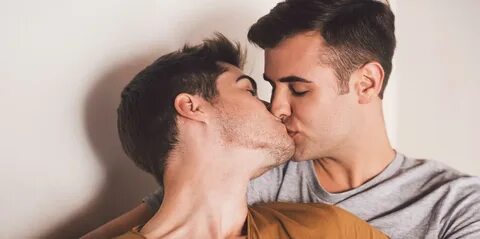 Affectionate young gay couple kissing while lying in bed together in the mo...