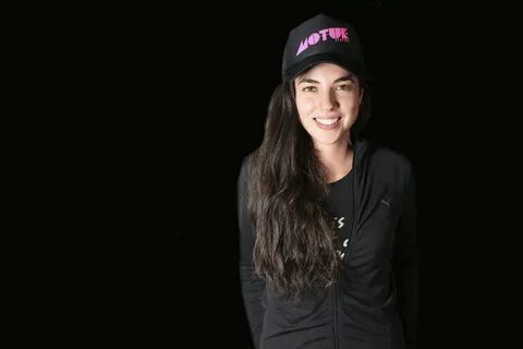 Smiling woman in a black outfit and 'VOTE' cap posing for a HD de...