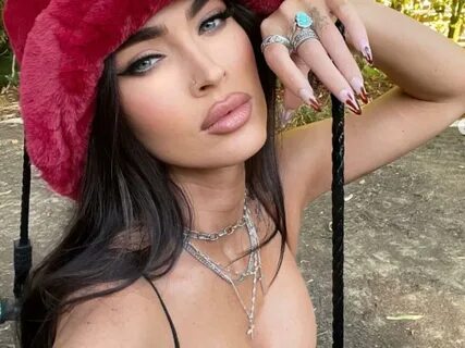 Megan Fox con sombrero rojo y mano en mejilla, pecho descubierto. 