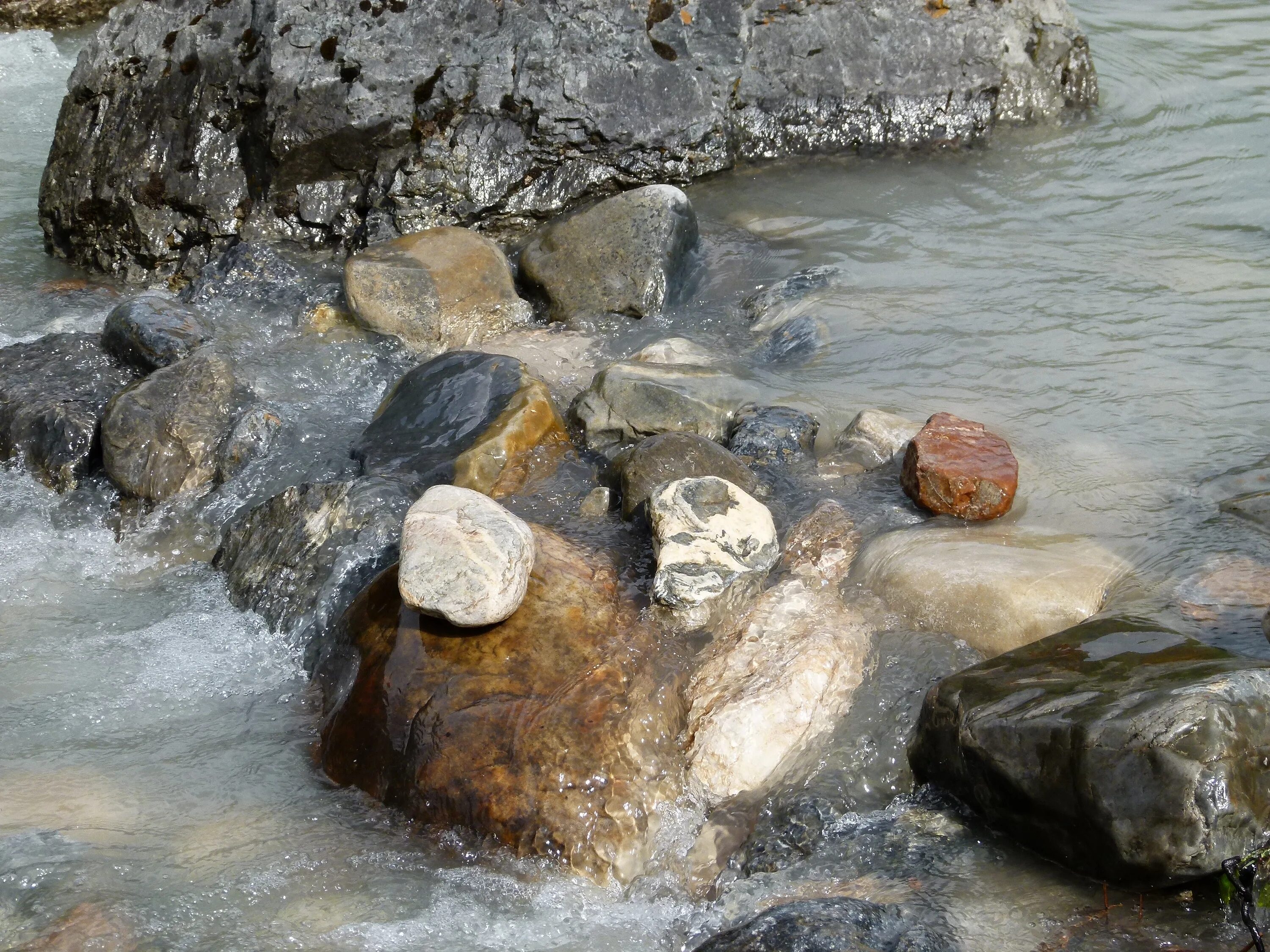 Изменения в течении ручья. Ручей с камнями. Зеленые гладкие камни в ручье. Вода течет по камням.