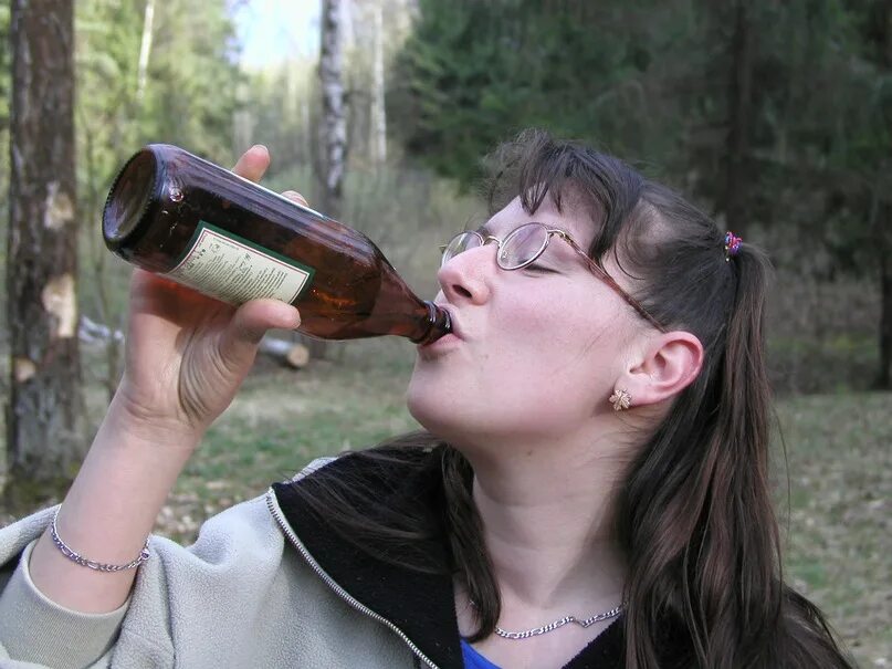 Девушка пьет пиво из бутылки.