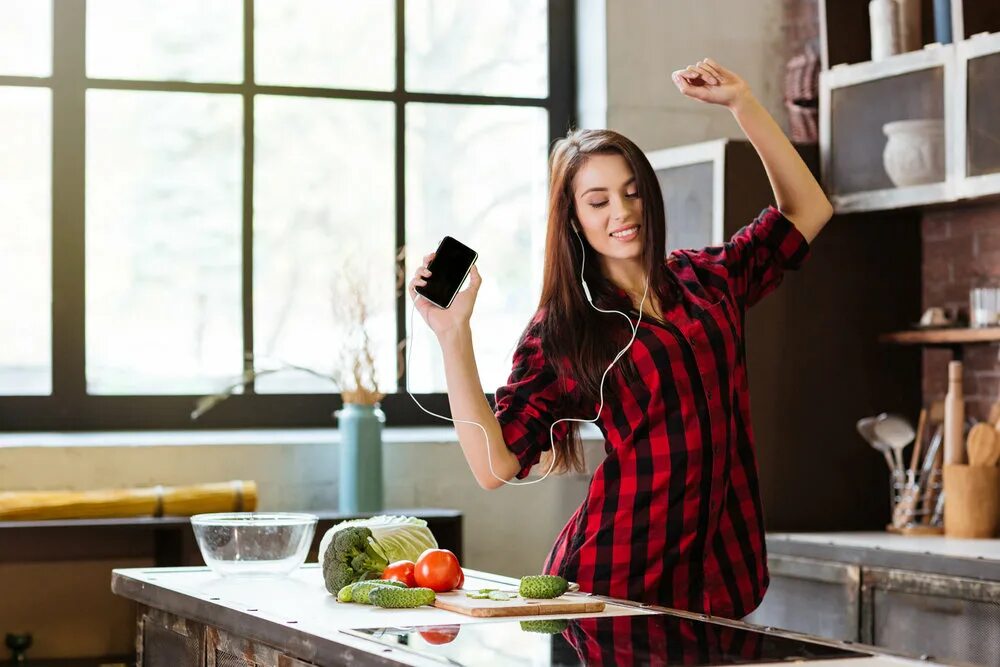 Танцы на кухне. Женщина танцует на кухне. Женщина со смартфоном на кухне. Красивая девушка на кухне.