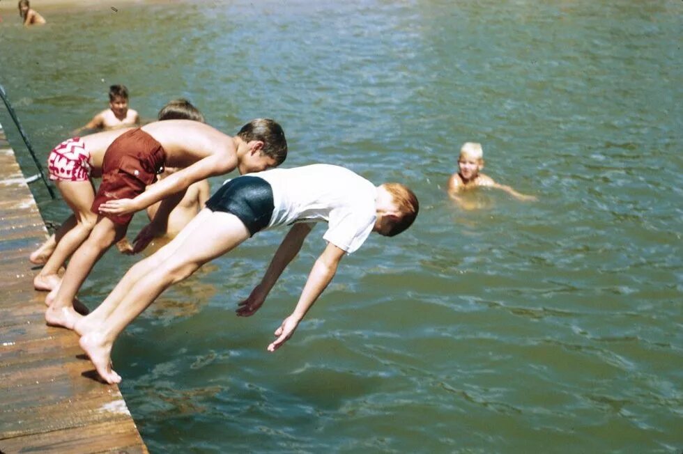 В воде ныряет в реку. Дети плавают в реке. Мальчик ныряет.