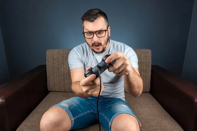 А как в приставку играть. Мужчина играет в приставку. man playing game console. фото играем в приставку. диван с пультом.